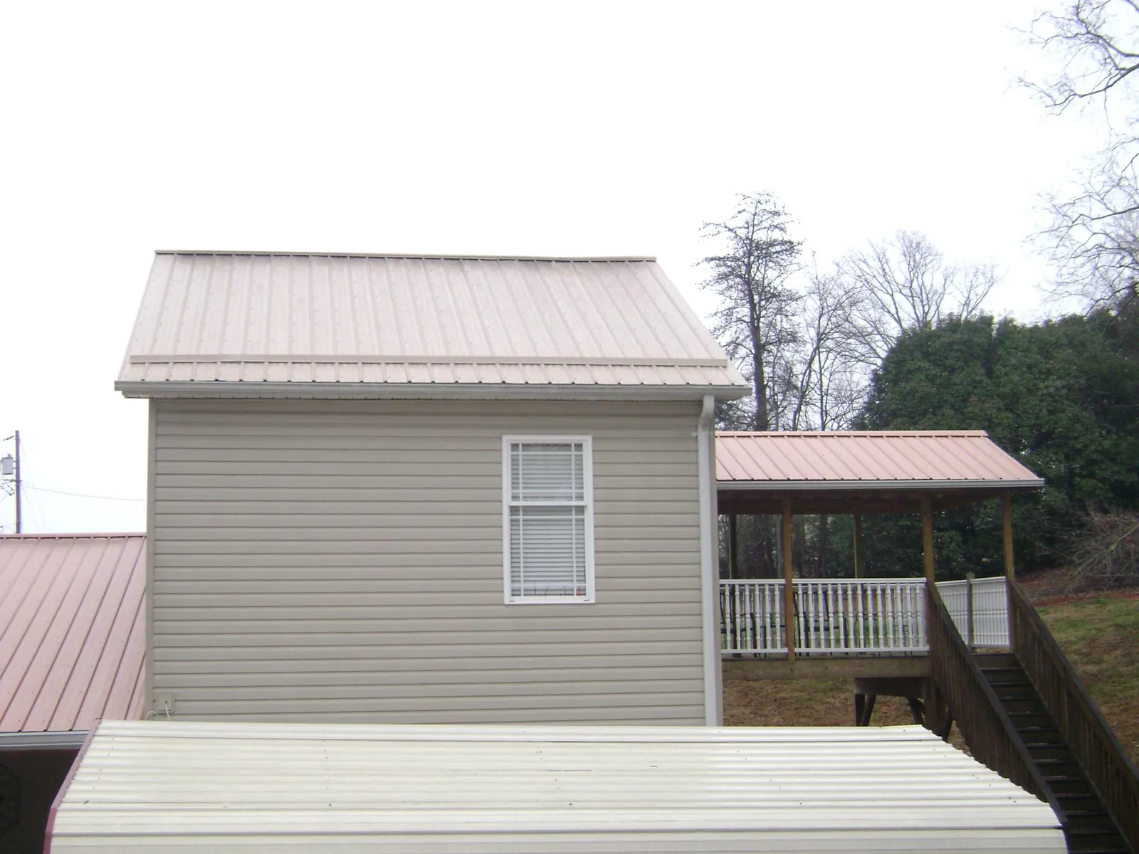 Tan metal roofs on a two story addition and attached porch, from a Roof Replacement job in Midway